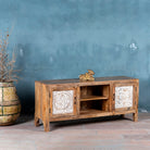 Side angle view of a mango wood low board featuring hand-carved floral motif doors with whitewashed detailing, open central shelving, and a warm natural wood finish.