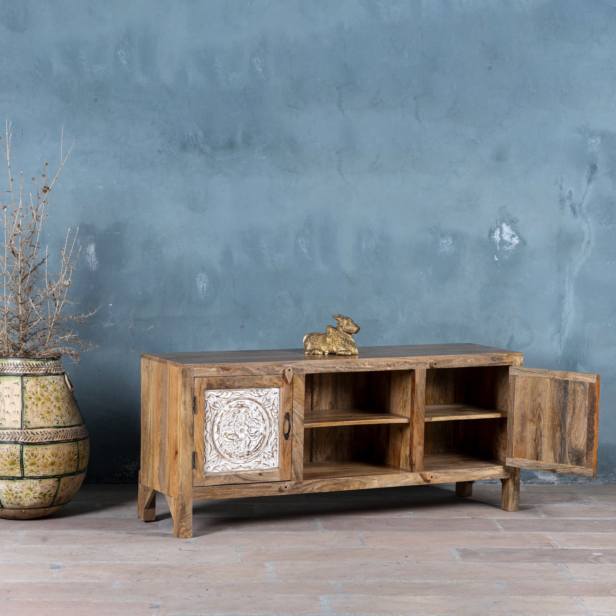 Mango wood low board featuring hand-carved floral motif doors with whitewashed detailing, open central shelving, and a warm natural wood finish.