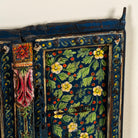 Close up image of a decorative wall panel made from an old teak wood window frame, hand-painted with intricate floral patterns in vibrant colours including green, red, yellow, and blue, showcasing traditional Indian craftsmanship and vintage charm.
