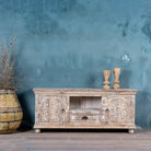 Low board made from solid mango wood with intricately hand-carved circular floral doors, distressed white finish, and central open shelf with drawer for functional storage.