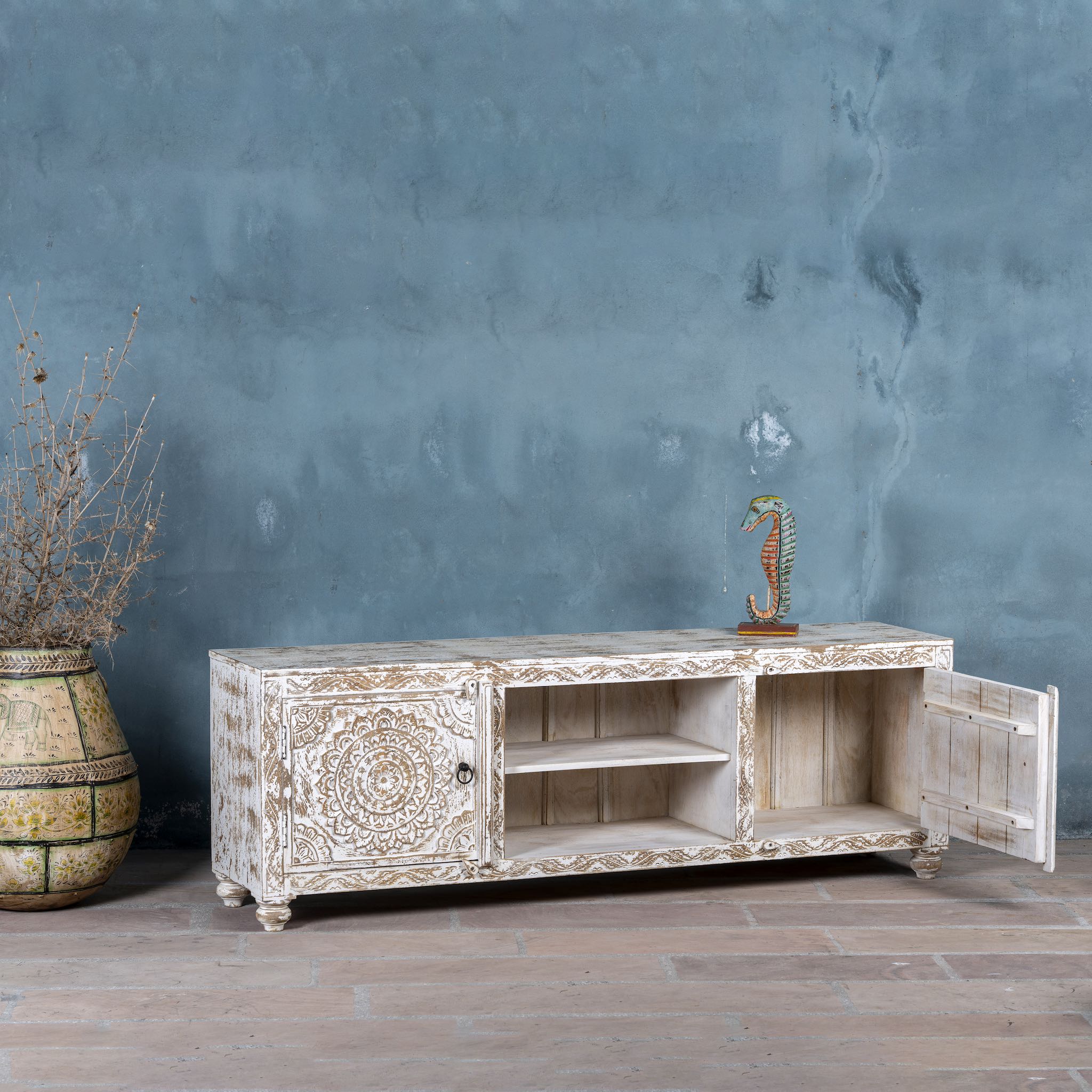 Wooden console table with intricate carvings against a textured blue wall.