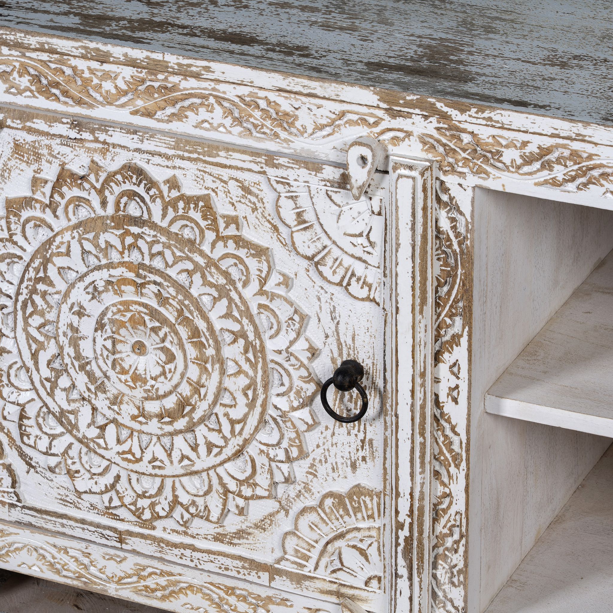 Close up picture of a low board made from solid mango wood, featuring intricate hand-carved mandala motifs, whitewashed finish, and practical storage with two doors and open shelving.