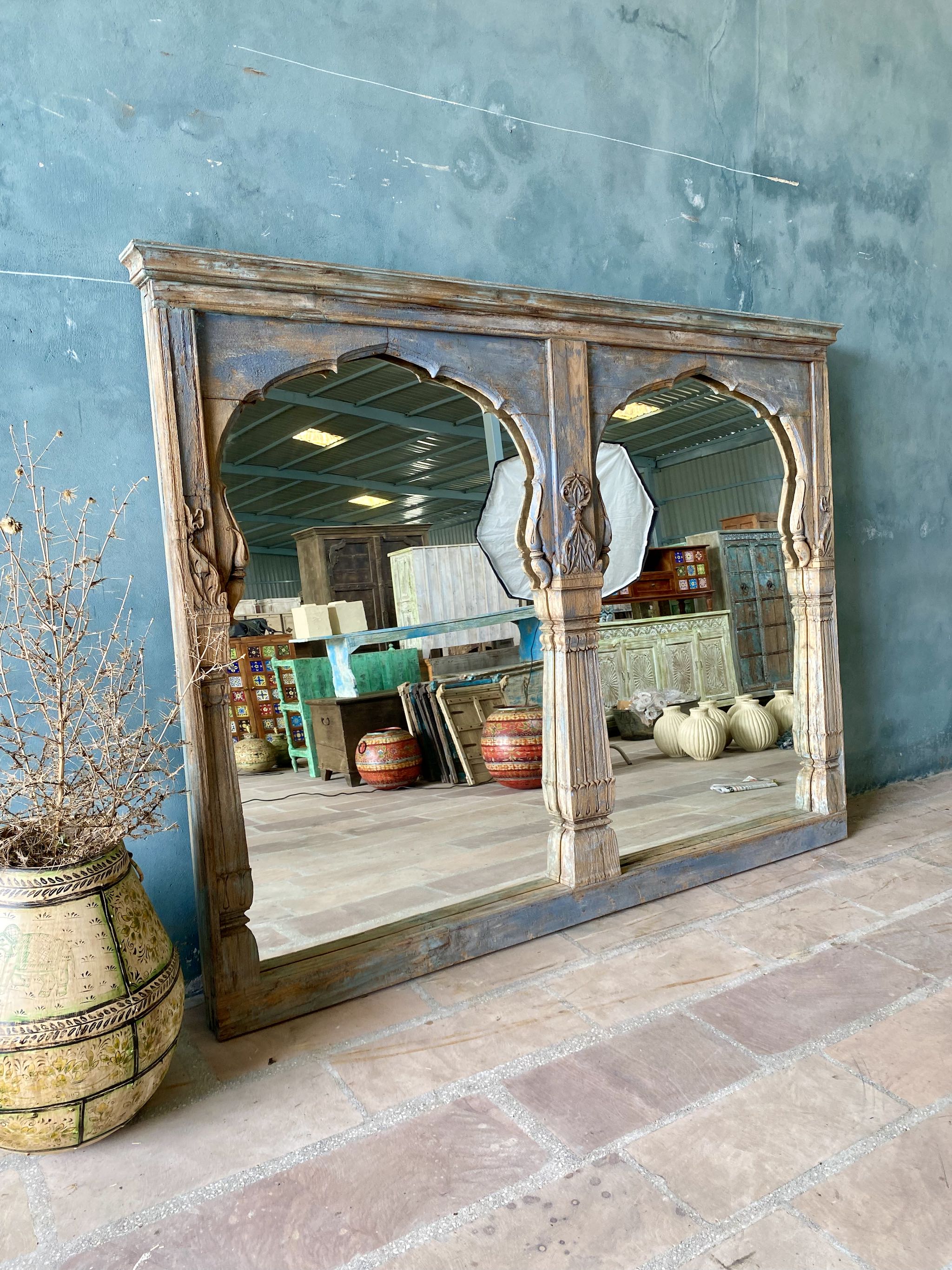 Life style picture of a vintage two-arch mirror crafted from reclaimed teak wood, with hand-carved details and a weathered blue patina finish.