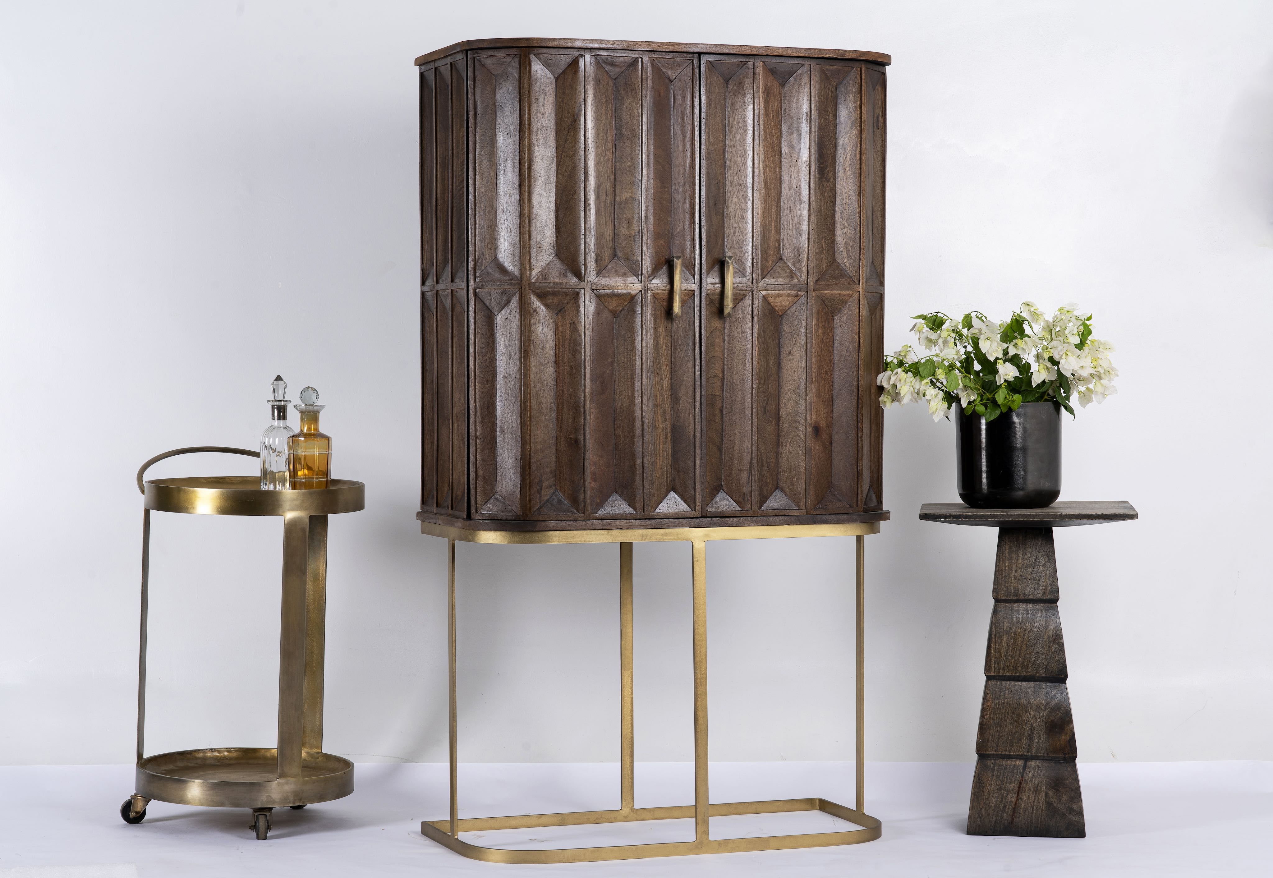 Side angle image of a tall mango wood cabinet with diamond tile carving, bronze handles, and black metal base, 86 × 42 × 150 cm.