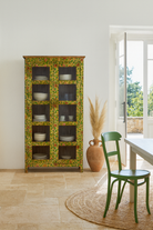 Lifestyle image of a hand-painted reclaimed wood showcase cabinet with floral motifs and glass doors, sustainable furniture and vintage home decor style, 96 × 40 × 182 cm.
