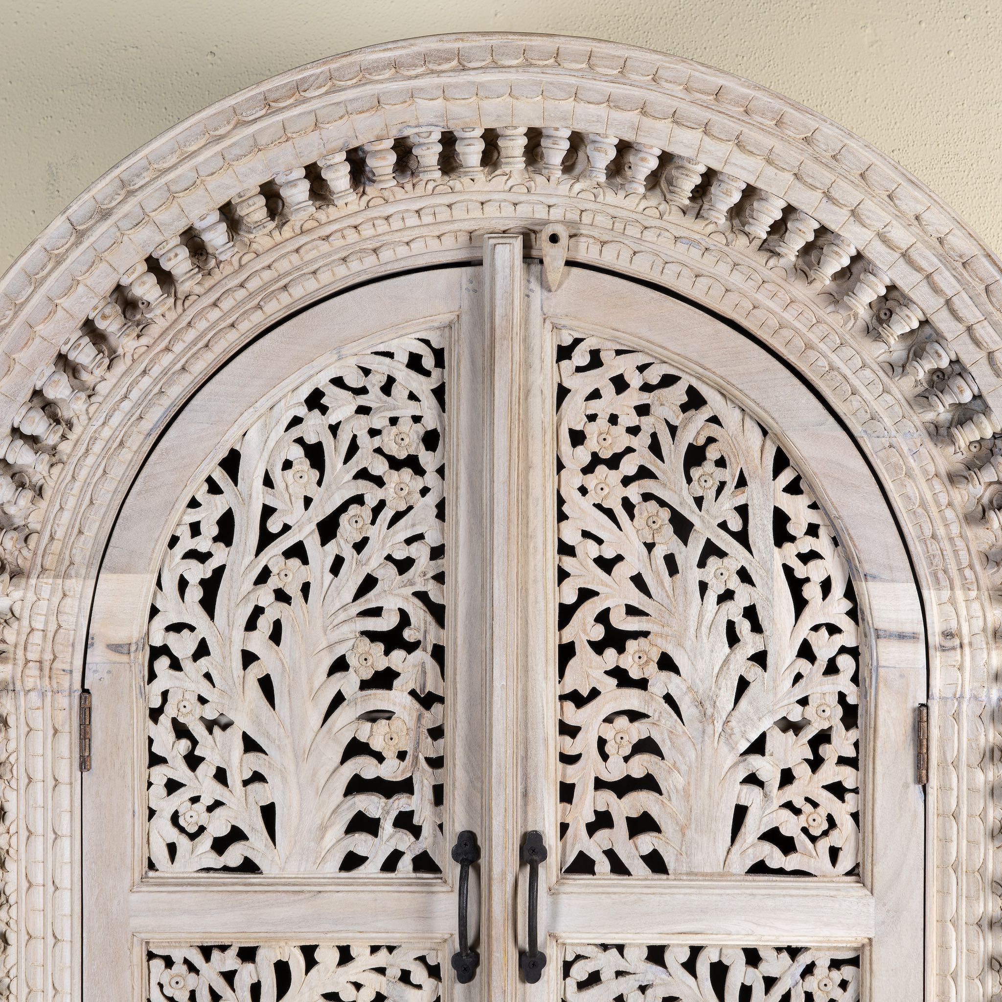 Close up picture of a mango wood cabinet with intricately hand-carved doors and an arched half-round top, showcasing a detailed tree motif and traditional Indian craftsmanship.