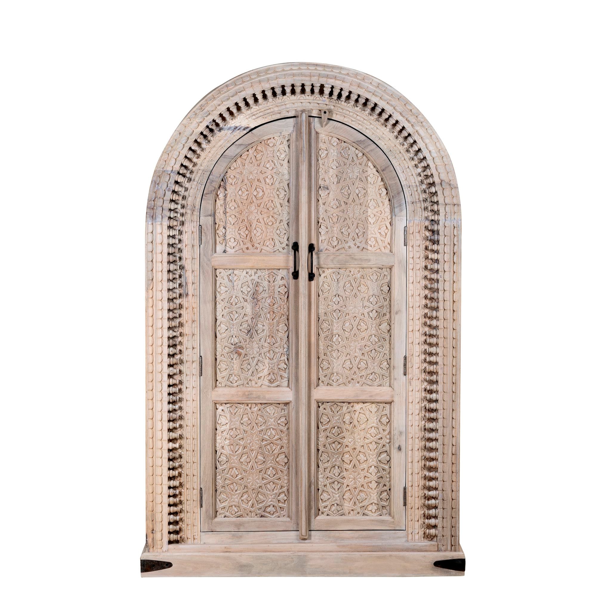 White background picture of a hand-carved mango wood cabinet with an arched half-round top and ornate closed floral pattern doors, finished in a soft natural tone for timeless elegance.