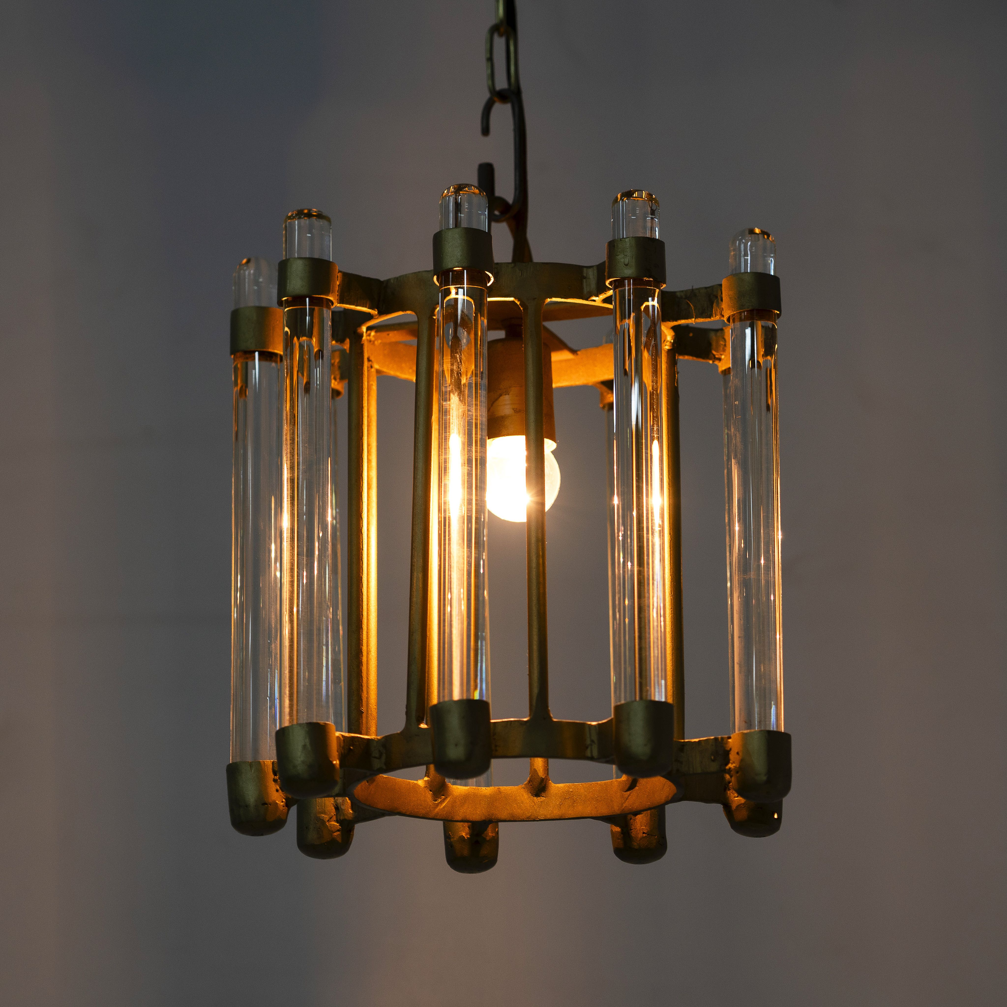Lighted version of a round antique brass iron and glass pendant light with test tube shade – minimalistic pendant light ideal for soft glass lighting in bedrooms, kitchens, or entryways.