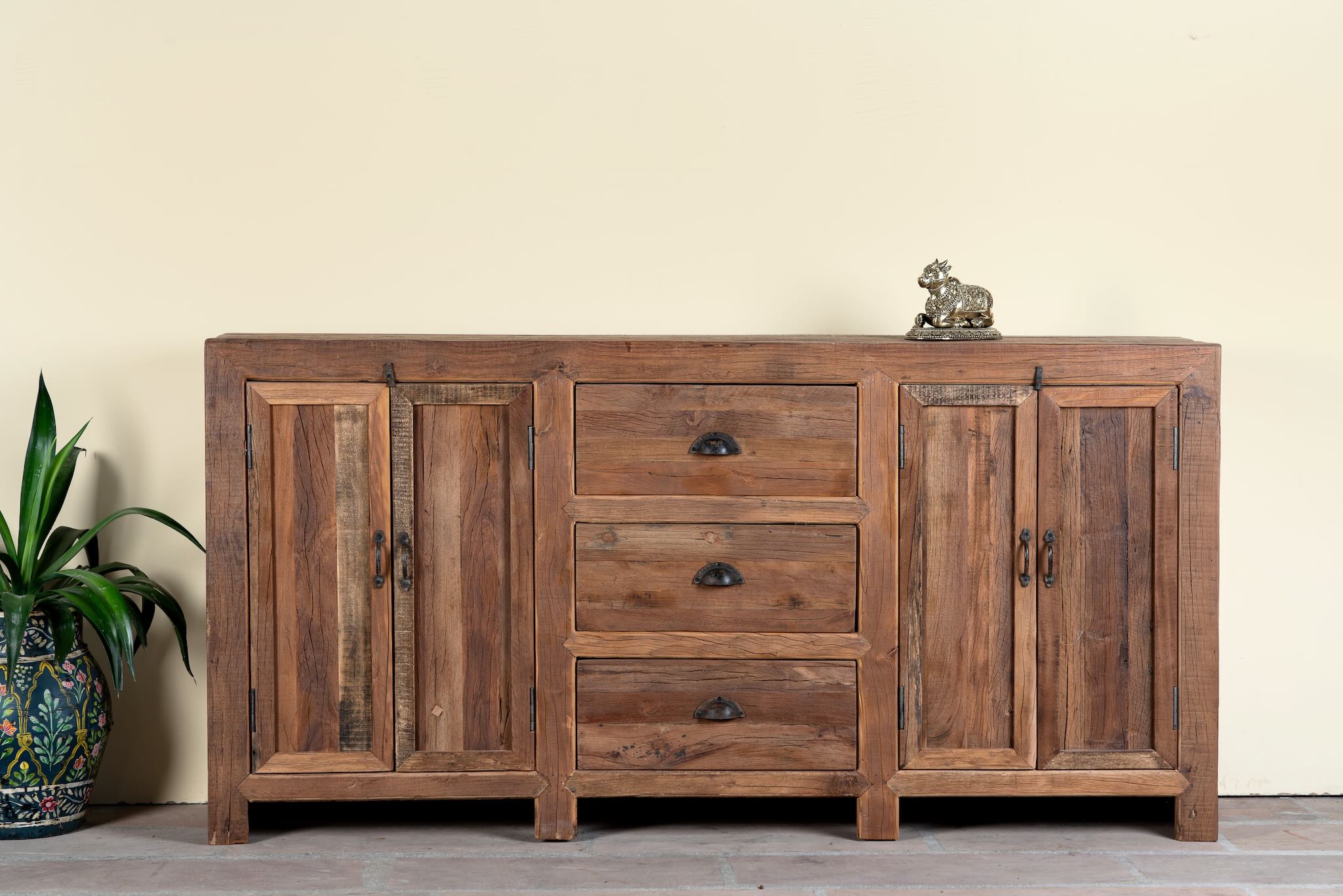 Reclaimed wood sideboard Avika in a rustic minimalistic design with three drawers and two double-door cabinets. A sustainable furniture piece with warm wood tones and black iron handles, perfect for eco-conscious interiors.
