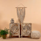 A pair of vintage design hand-carved bedside tables made from natural mango wood, with a tree motif, displayed with a rattan hanging planter and other decorative items on a neutral background.