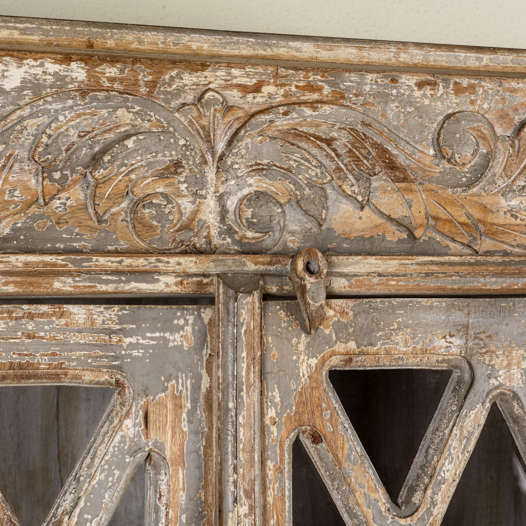 Close up image of a handcrafted showcase cabinet made from reclaimed wood, featuring diamond-pattern glass pane doors, a crackled paint finish in earthy tones, two drawers, and vintage-inspired detailing.