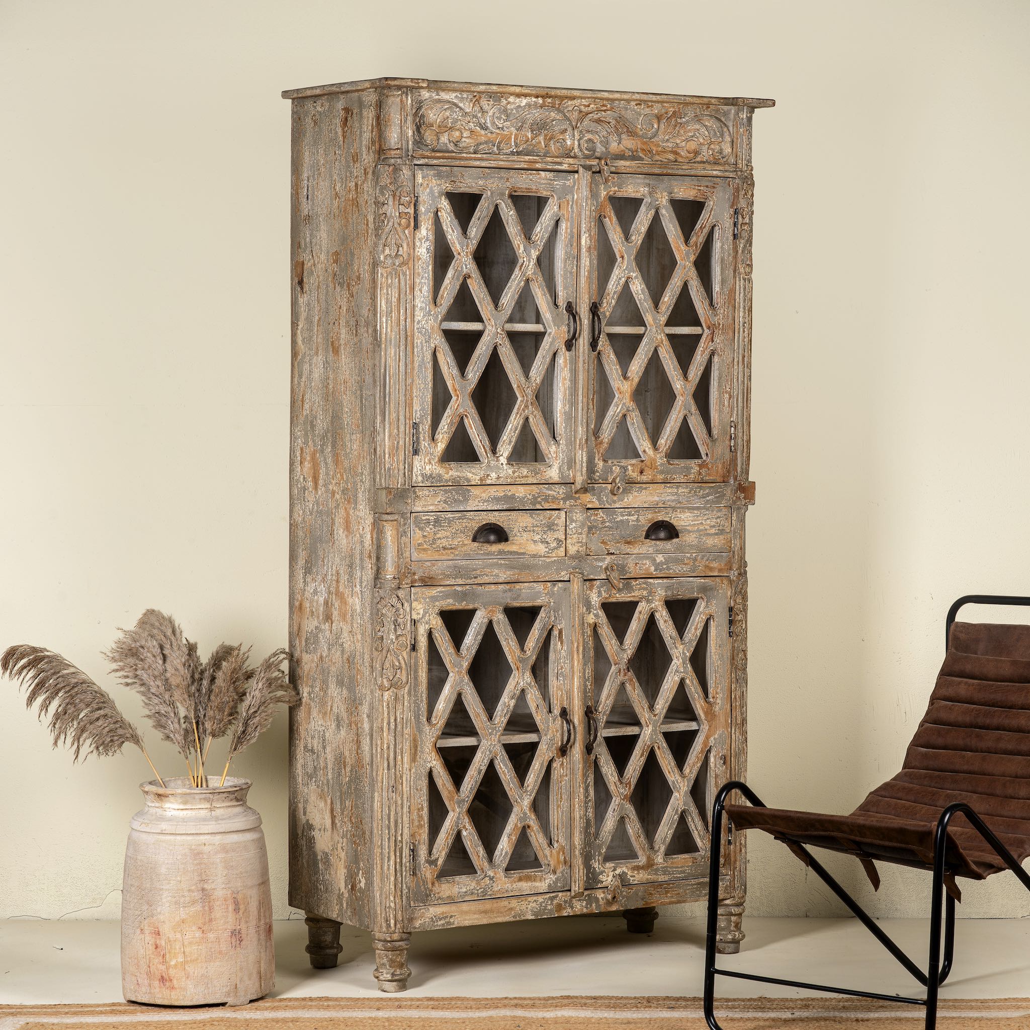 Side angle image of a handcrafted showcase cabinet made from reclaimed wood, featuring diamond-pattern glass pane doors, a crackled paint finish in earthy tones, two drawers, and vintage-inspired detailing.