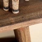 Close up image of a console table crafted from reclaimed teak wood, featuring a minimalist rustic design with angled legs and a lower shelf, showcasing the natural grain, texture, and character of the weathered wood.
