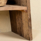 Close up image of a table leg of a console table crafted from reclaimed teak wood, featuring a minimalist rustic design with angled legs and a lower shelf, showcasing the natural grain, texture, and character of the weathered wood.
