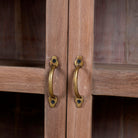 Close up image of the handles of a  rustic showcase cabinet made from recycled teak wood, featuring four glass-paneled doors with brass handles and a lightly weathered finish, offering a warm, natural look ideal for displaying decor or tableware.
