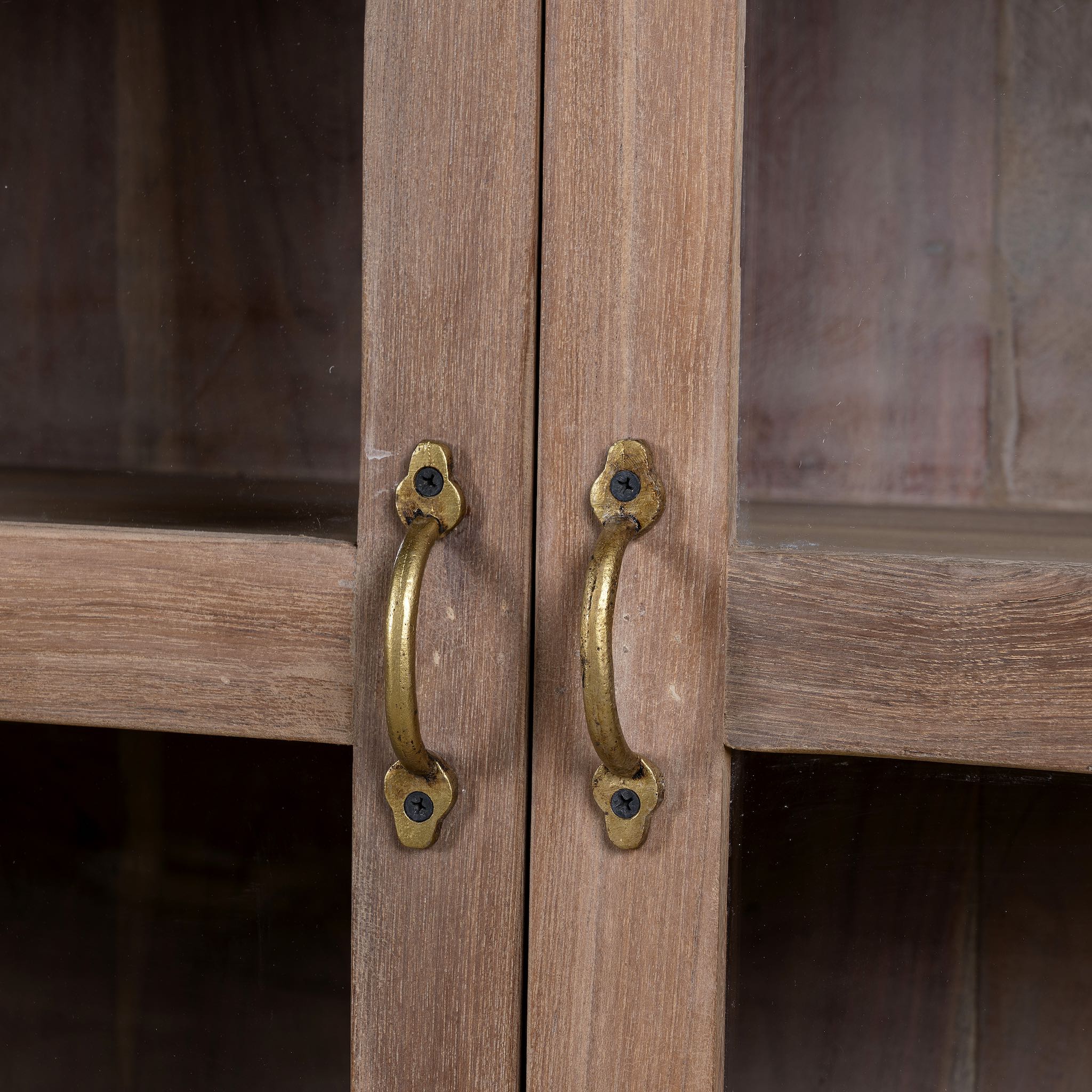 Close up image of the handles of a  rustic showcase cabinet made from recycled teak wood, featuring four glass-paneled doors with brass handles and a lightly weathered finish, offering a warm, natural look ideal for displaying decor or tableware.
