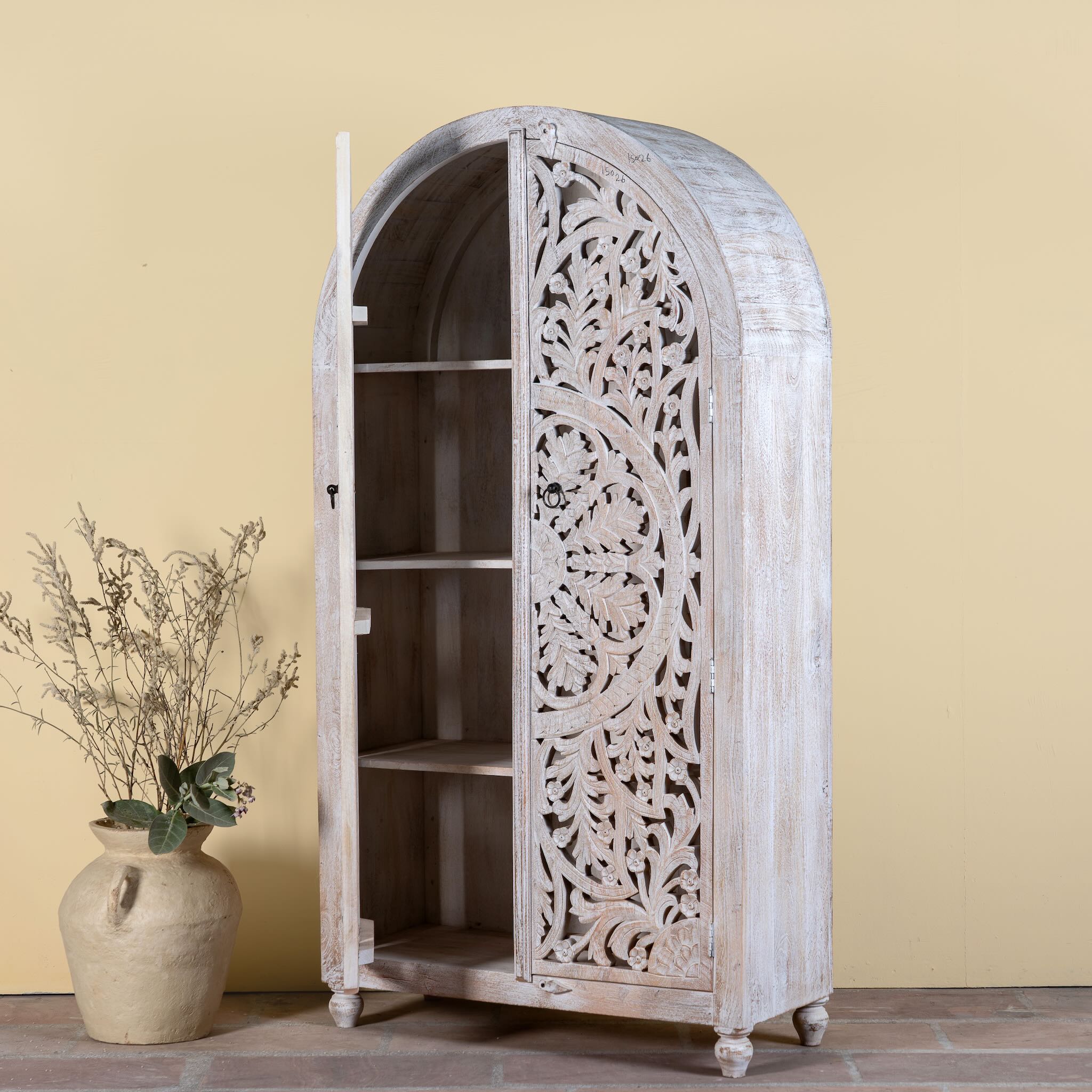 Side angle image with open doors of a Bhuvana arched mango wood wardrobe featuring a sculptural half-round design, intricate hand-carved floral detailing, and carved legs—an artisanal piece in the collection of arched wardrobes and mango wood wardrobes.