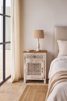 Lifestyle scene of a pair of carved nightstands made from mango wood with geometric patterns and distressed finish; perfect bedroom furniture, 76 × 56 × 35 cm.