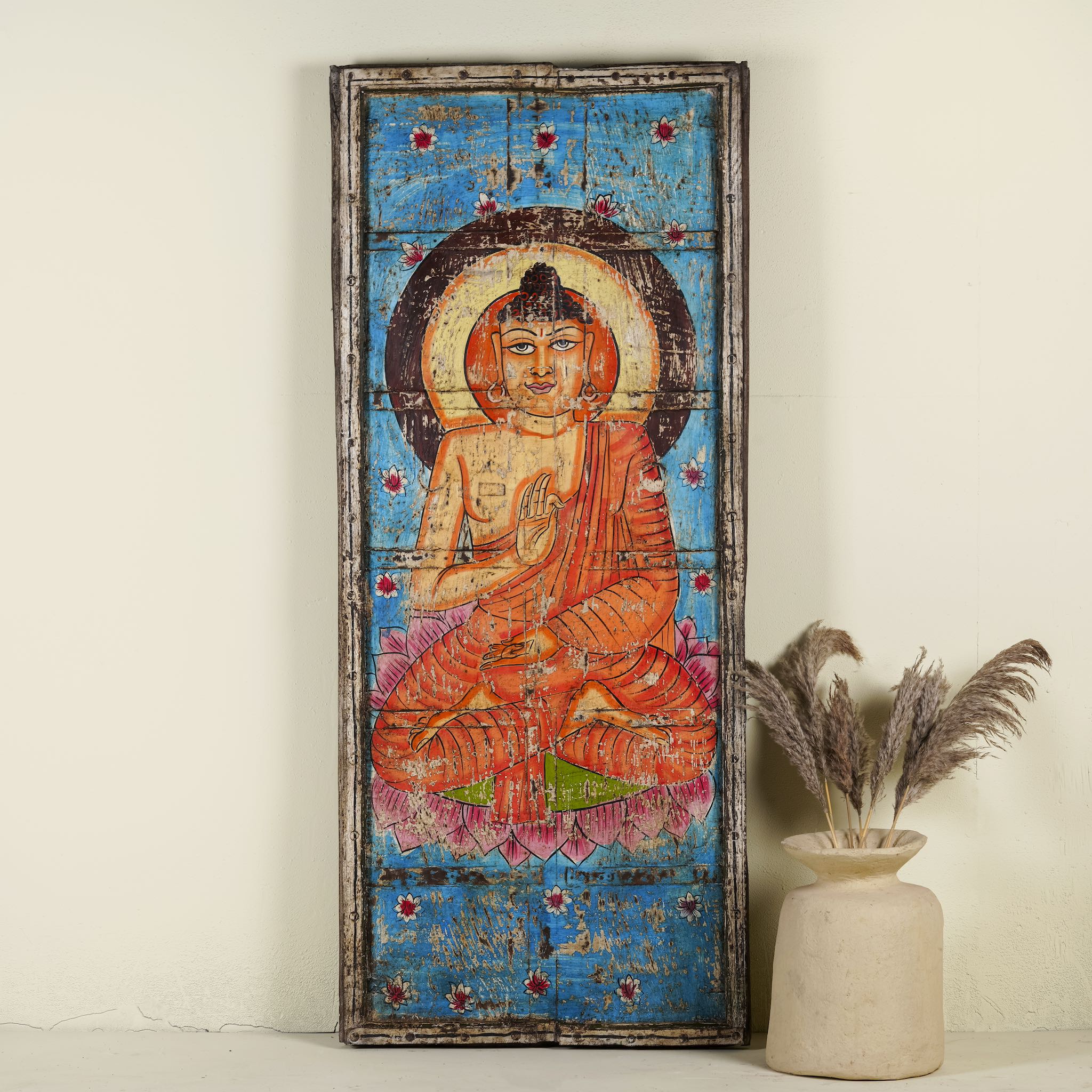 Hand-painted wall panel made from reclaimed wood, featuring a vibrant depiction of Buddha in a meditative pose on a lotus flower, with a bright blue floral background and a worn, rustic finish that adds vintage charm.
