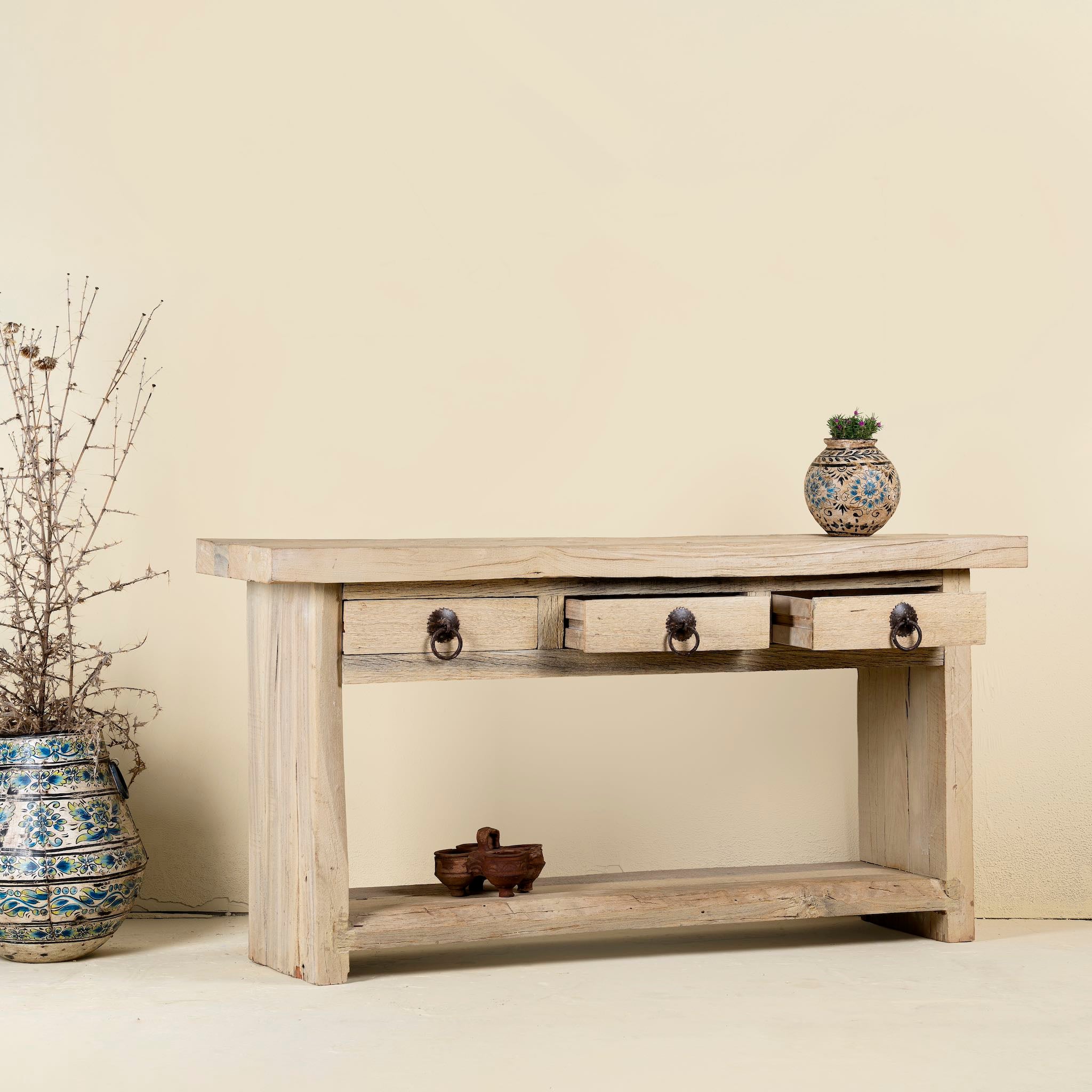 Open drawer image of a rustic console table crafted from reclaimed teak wood, featuring a natural weathered finish, three drawers with metal ring pulls, and a lower shelf for additional storage or display, blending simplicity with organic charm.
