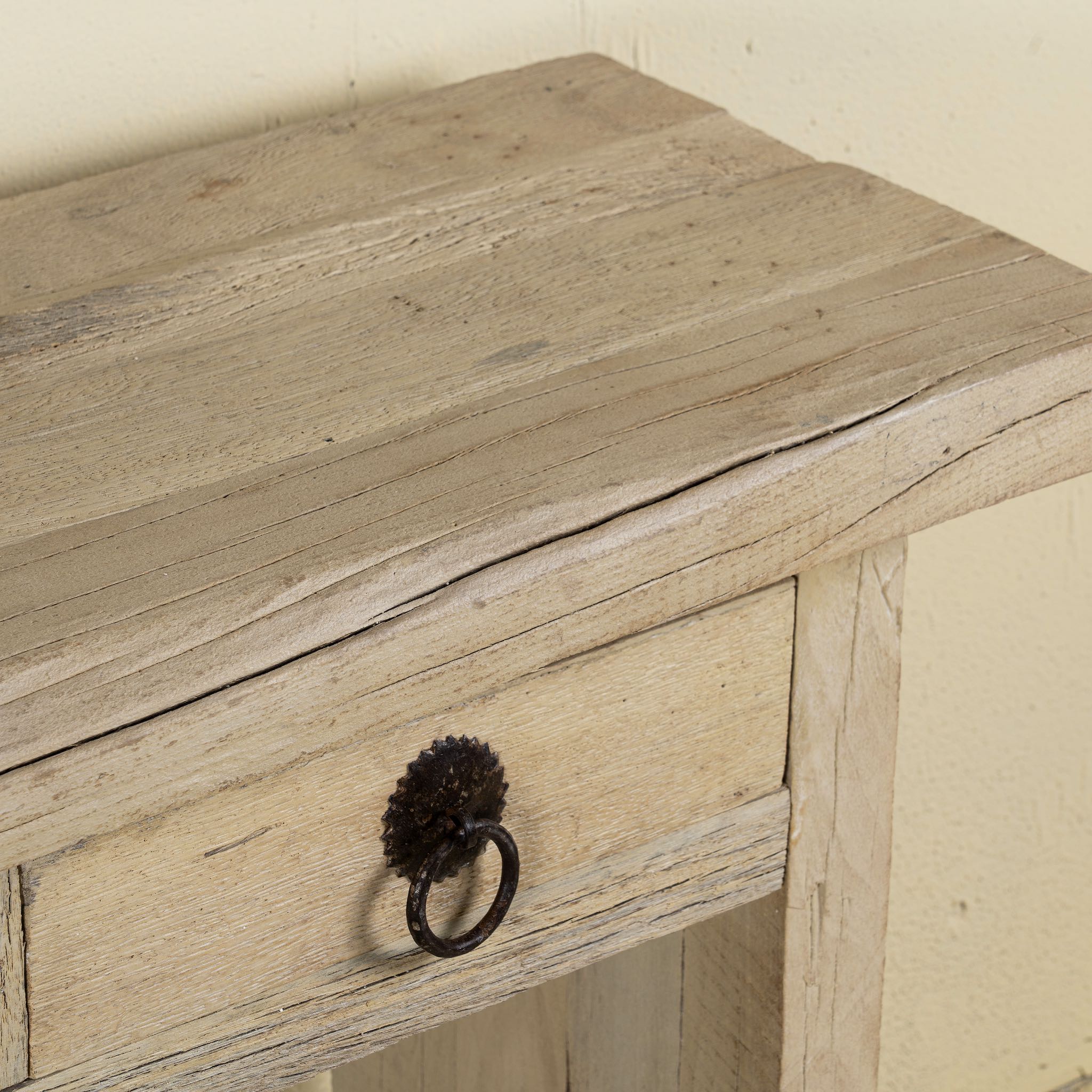 Close up image of a rustic console table crafted from reclaimed teak wood, featuring a natural weathered finish, three drawers with metal ring pulls, and a lower shelf for additional storage or display, blending simplicity with organic charm.
