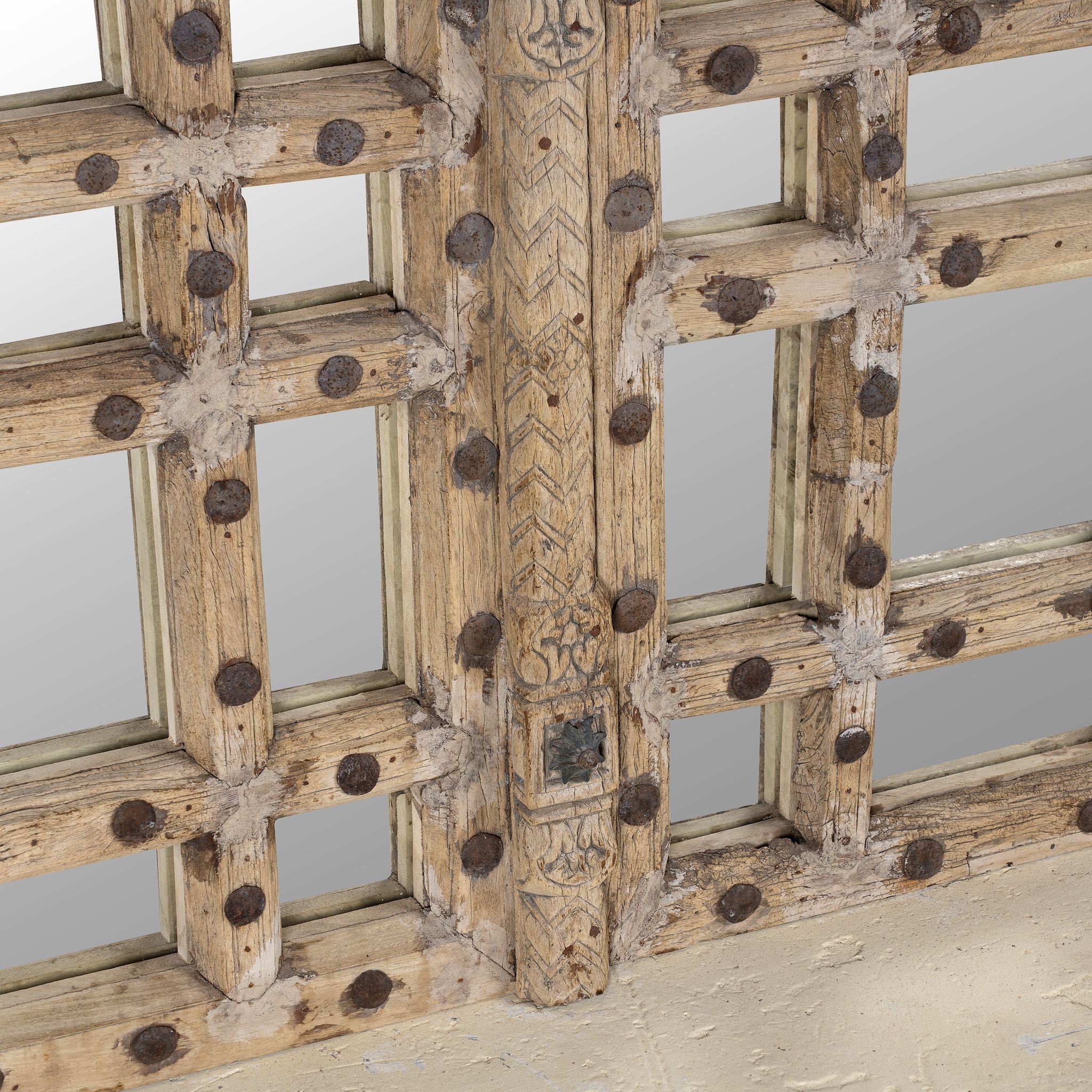 Close up of a statement wall mirror made from an old teak window frame with large square grid pattern, metal studs, and decorative center carving-  a bold blend of rustic charm and historic craftsmanship.