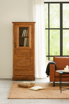 Lifestyle image of a antique teak wood display cabinet with glass door, shelves, and lower drawer – unique furniture piece crafted from teak wood with traditional Indian design and honey wax finish.