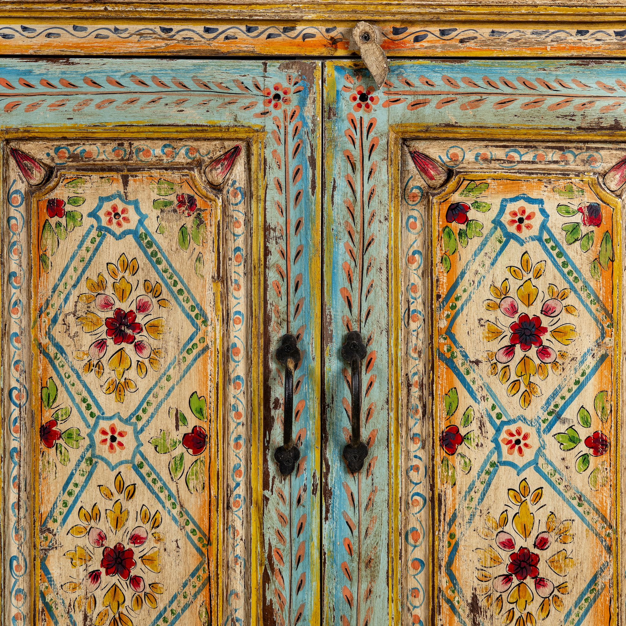 Close up image of a hand-painted sideboard made from reclaimed wood, featuring four intricately detailed doors with vibrant floral and geometric motifs in soft blues, yellows, and reds, finished with a distressed vintage patina for a charming, artisanal look.
