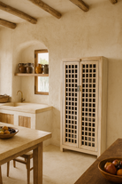 Life style image of a sandblasted mango wood showcase with two glass-panelled grid doors and four interior compartments, finished in a light sun-washed tone, ideal as living room furniture.