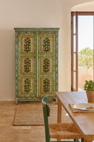 Lifestyle image of a Hand-painted reclaimed wood cabinet with floral motifs and green frame – Drisina by Om Home & Garden, a unique piece of sustainable furniture with bohemian flair.