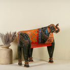 Side angle image of a elephant-shaped armchair crafted from reclaimed wood, featuring intricate hand-painted details in vibrant red, orange, green, and multi coloured floral patterns, with sculpted elephant head and legs for a whimsical, artistic touch.
