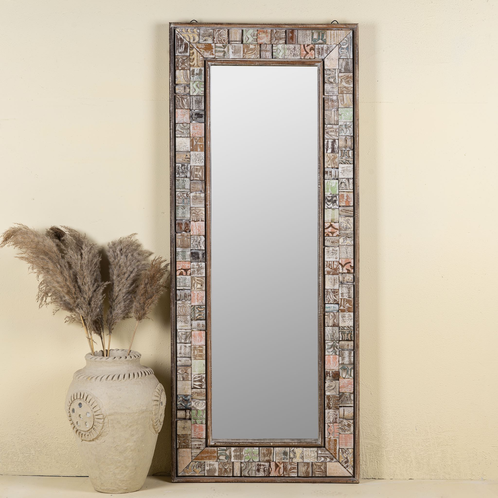 Front view image of a rectangular mirror framed with reclaimed wood, featuring a mosaic-style border of intricately carved and coloured wooden tiles, each with unique textures and patterns, creating a rustic and artistic statement piece.
