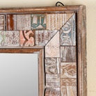 Close up image of a rectangular mirror framed with reclaimed wood, featuring a mosaic-style border of intricately carved and coloured wooden tiles, each with unique textures and patterns, creating a rustic and artistic statement piece.

