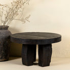 Front view of a rustic minimalistic style black coffee table made of reclaimed wood in front of a beige coloured wall.