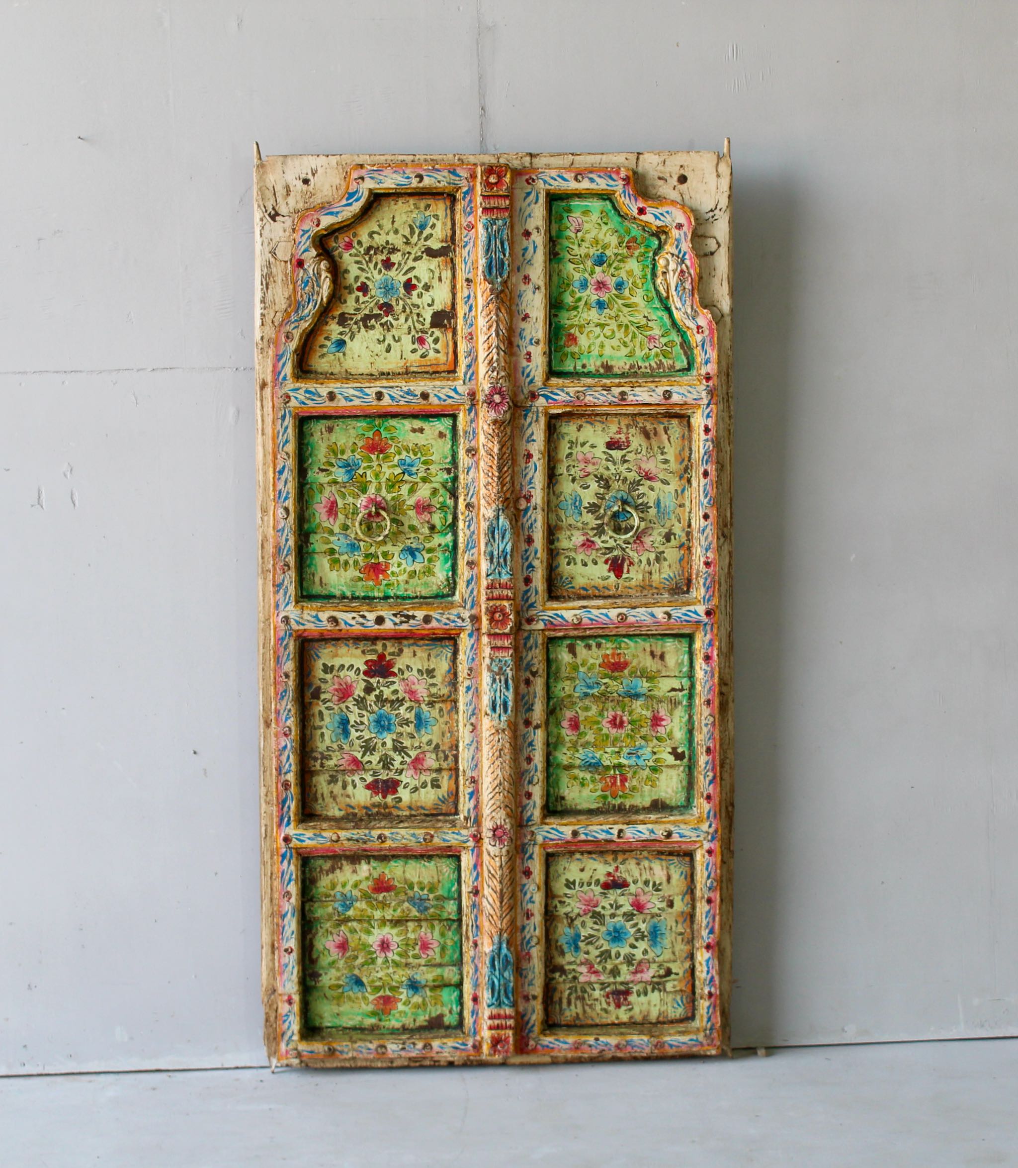 Gitra hand-painted teak door panel featuring floral motifs in soft pastels and a carved arched frame—an elegant and unique Indian wall decoration repurposed from antique architecture.