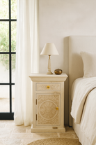 Lifestyle scene with a white washed pair of hand-carved nightstands made of sandblasted mango wood with floral Mediterranean patterns and one drawer – Hriday bedside tables by Om Home & Garden