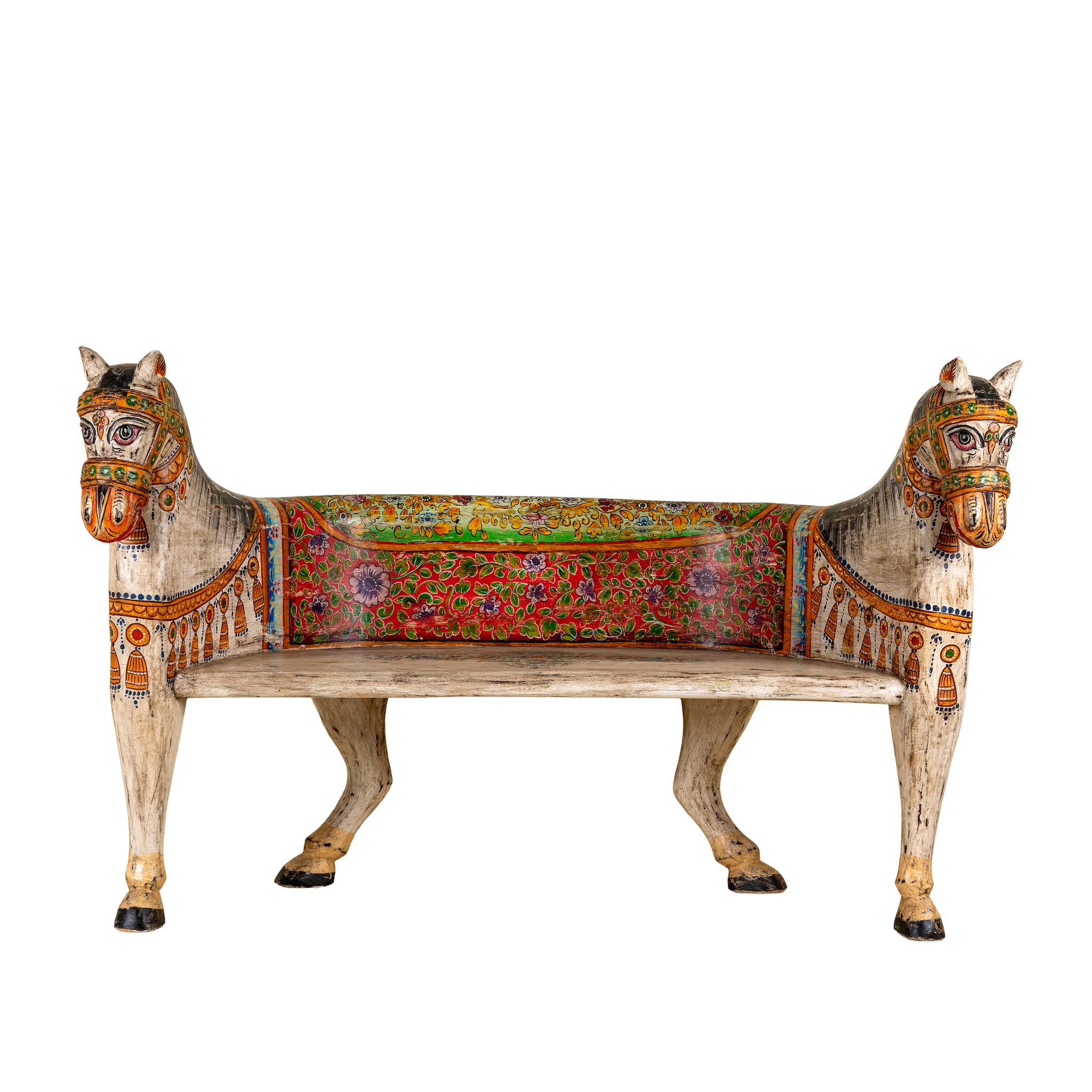 White background image of a hand-painted bench made from reclaimed wood, designed with intricately carved double horse heads at each end, featuring a vibrant floral backrest and detailed decorative patterns, blending traditional craftsmanship with whimsical artistry.
