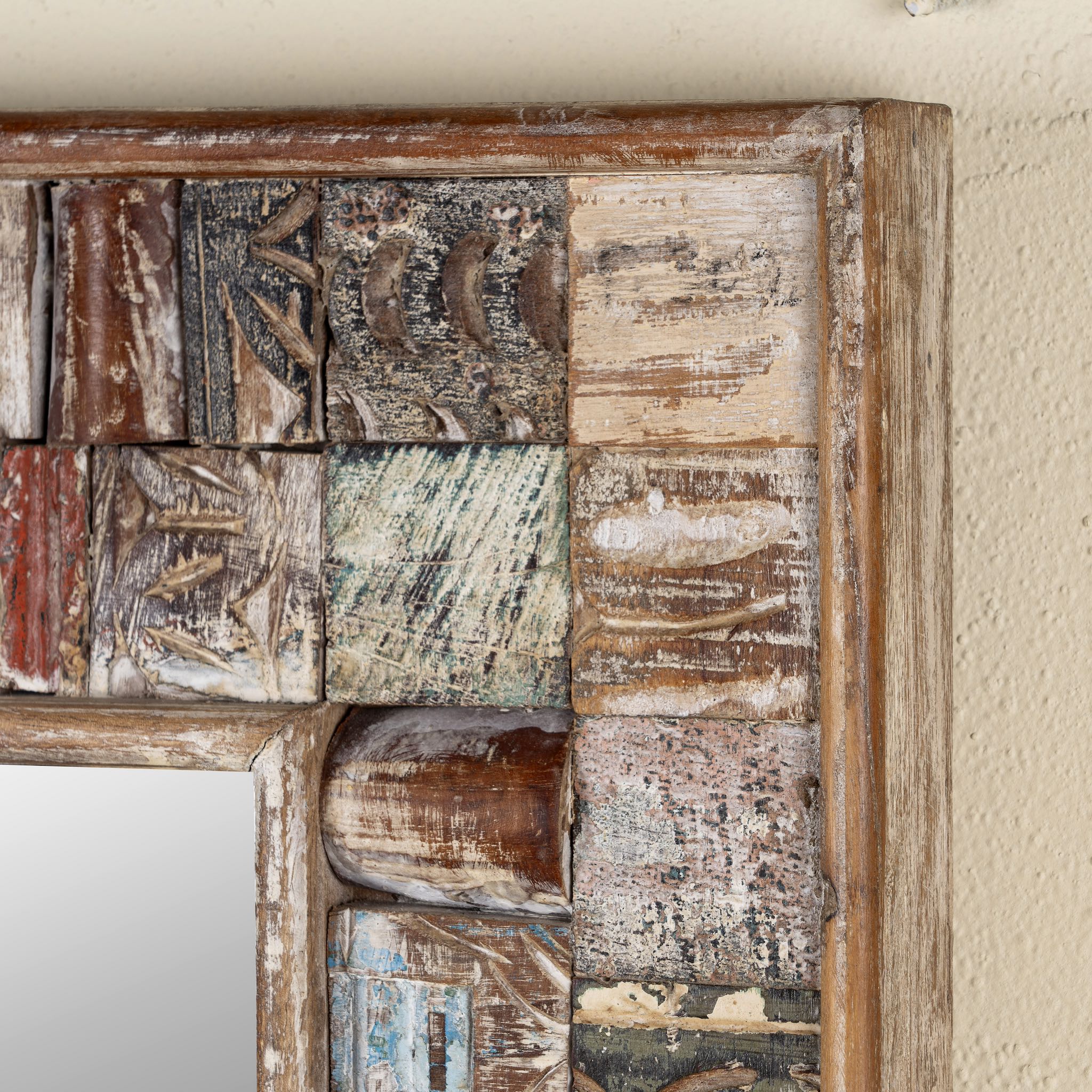 Close up image of a rectangular mirror framed with reclaimed wood, featuring a mosaic-style border of intricately carved and coloured wooden tiles, each with unique textures and patterns, creating a rustic and beautiful unique statement piece.

