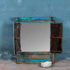 Vintage-style mirror with wooden frame and peeling blue paint against a textured gray wall.