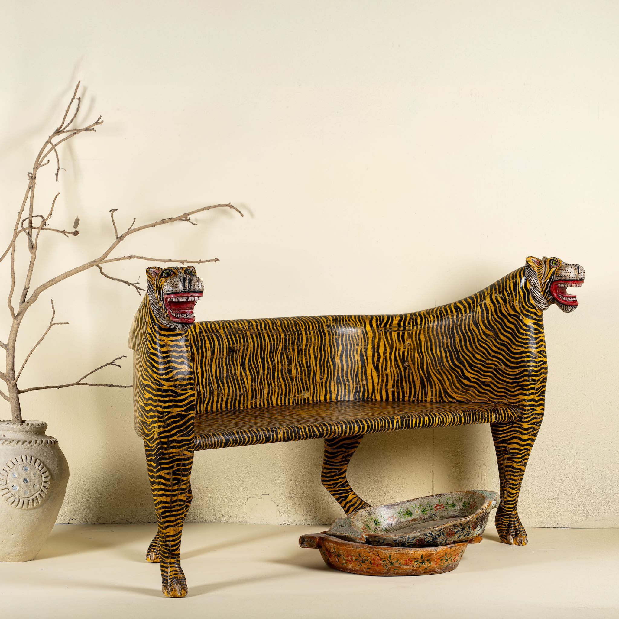 Front view image of a bold hand-painted bench made from reclaimed wood, designed with double tiger heads at each end and a vibrant yellow-and-black striped pattern throughout, combining whimsical animal form with striking folk-art flair.
