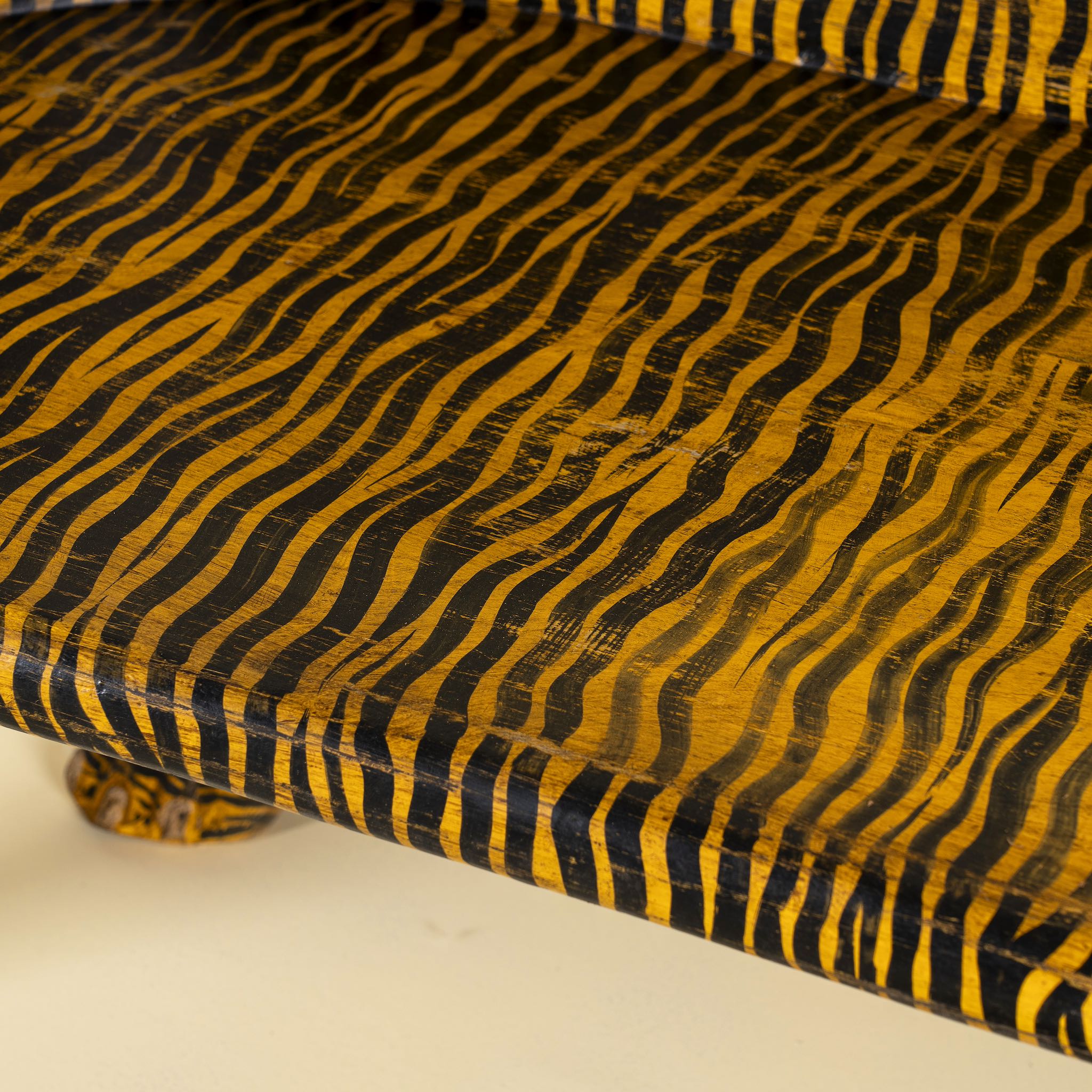 Close up image of a bold hand-painted bench made from reclaimed wood, designed with double tiger heads at each end and a vibrant yellow-and-black striped pattern throughout, combining whimsical animal form with striking folk-art flair.
