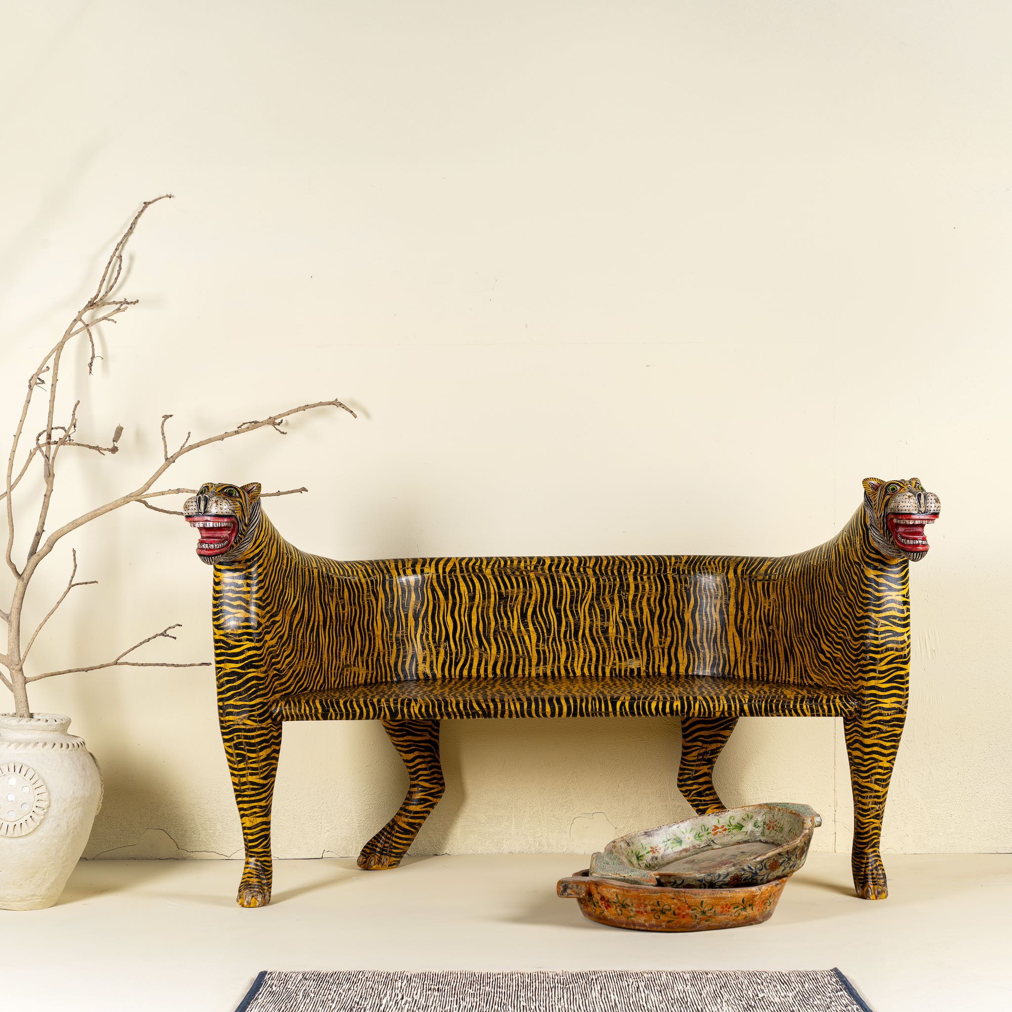 Bold hand-painted bench made from reclaimed wood, designed with double tiger heads at each end and a vibrant yellow-and-black striped pattern throughout, combining whimsical animal form with striking folk-art flair.
