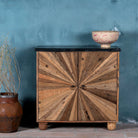 front view image of a rustic-style cabinet made from reclaimed wood, featuring a striking sunburst pattern on the double doors, round metal pulls, and a contrasting black marble top that adds a refined touch to its natural, weathered look.
