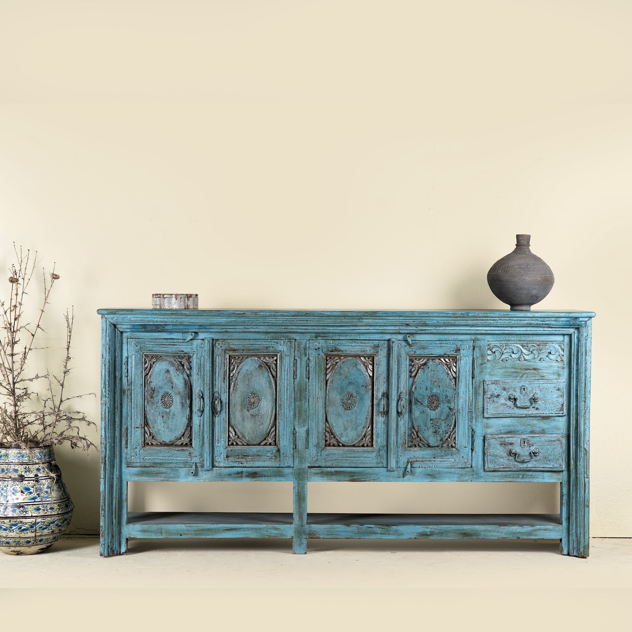 Antique console table made from solid teak wood, featuring four carved doors, three drawers, and a striking distressed turquoise finish for bold vintage flair.