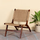 Side angle image of an acacia wood chair with handwoven cotton rope seat and backrest; rustic wooden armchair for living rooms or lounges, 60 × 80 × 95 cm.