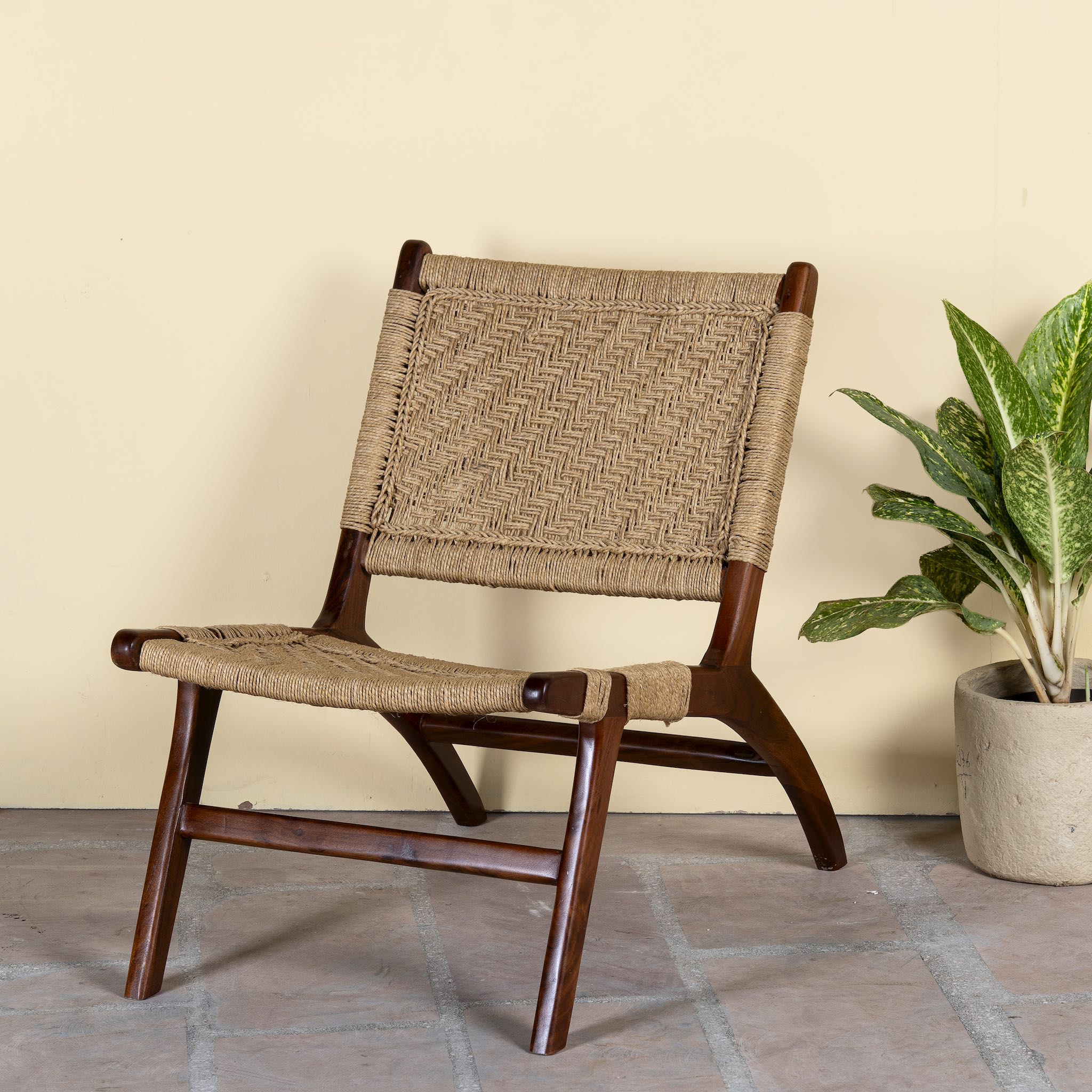Side angle image of an acacia wood chair with handwoven cotton rope seat and backrest; rustic wooden armchair for living rooms or lounges, 60 × 80 × 95 cm.