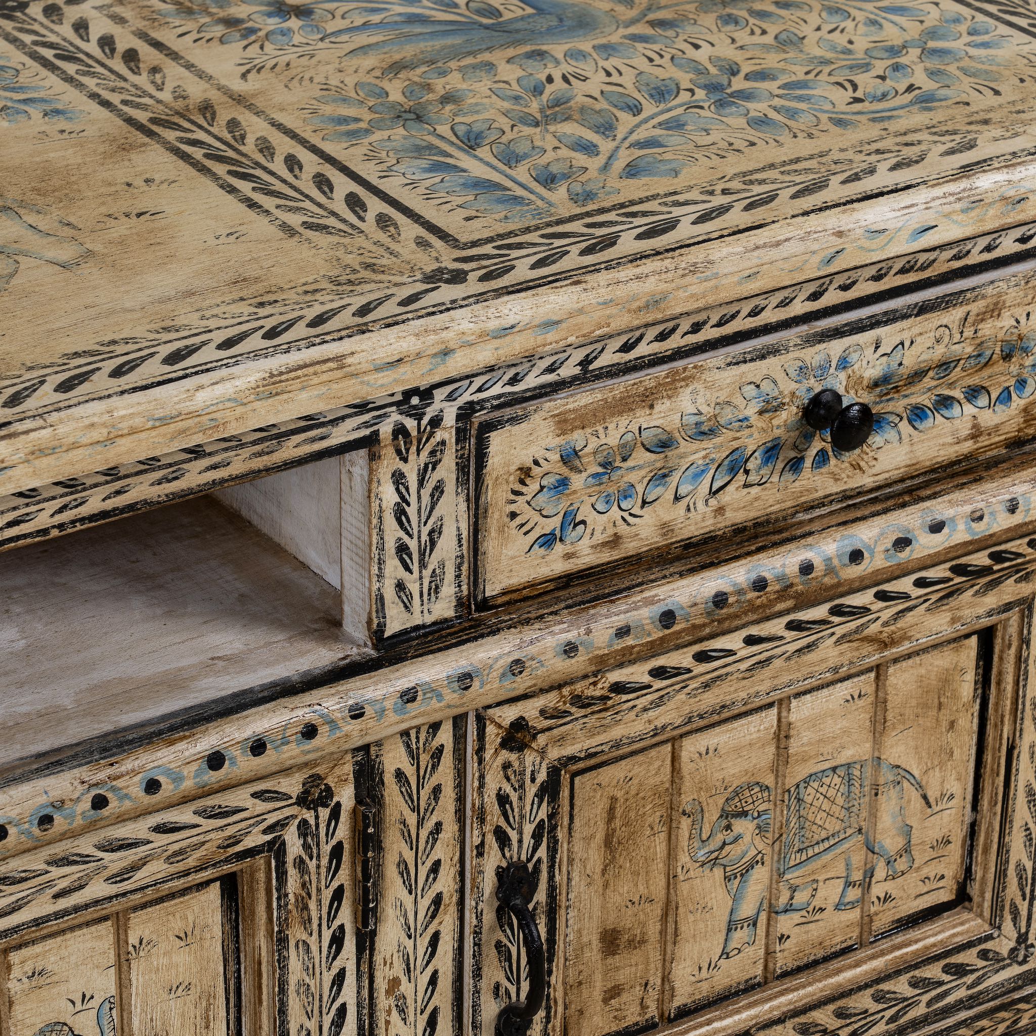 Close up image of a hand-painted lowboard made of reclaimed wood with traditional Indian animal motifs, featuring drawers and cabinets for storage, rustic finish, and artisanal detailing.
