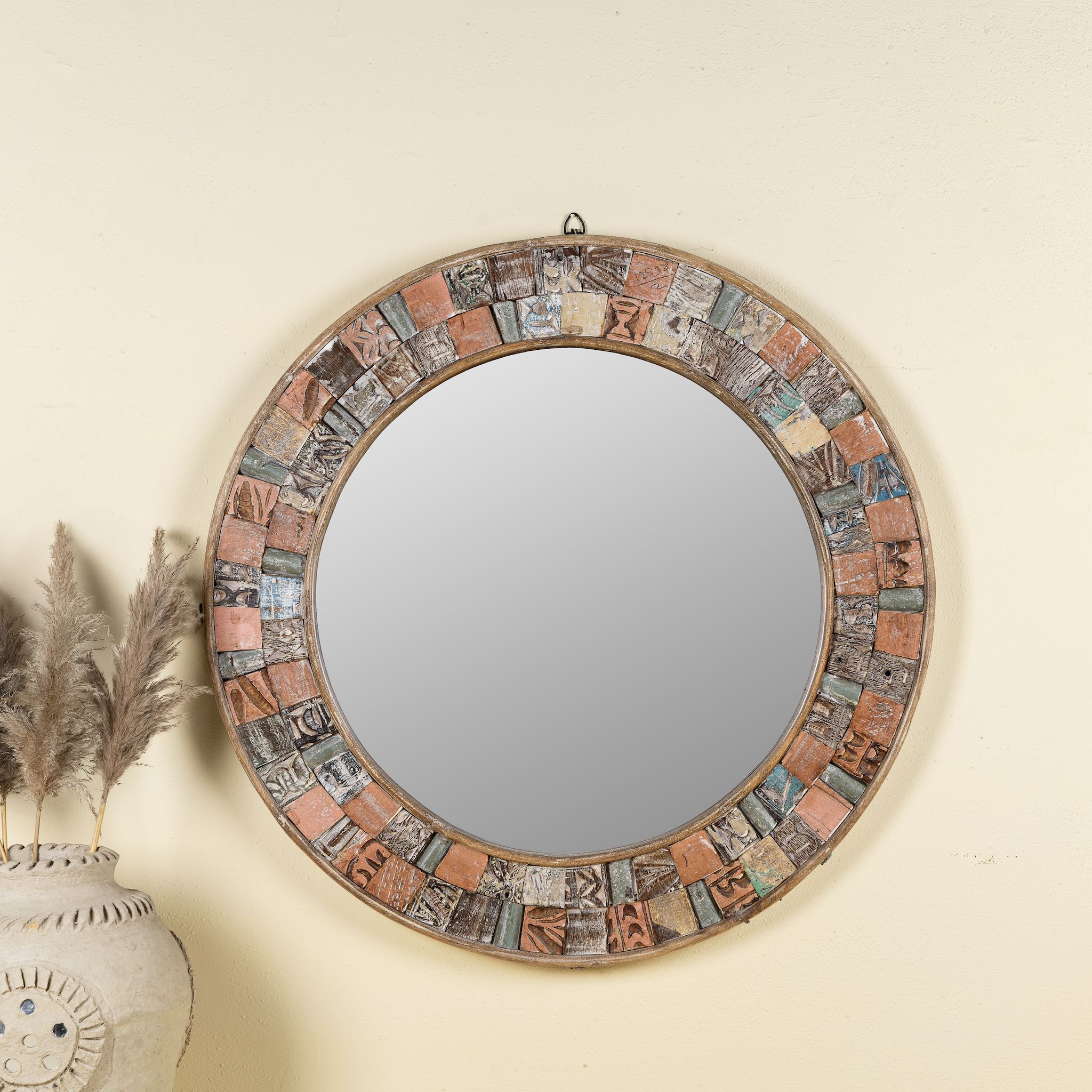 Front view image of a round mirror framed with reclaimed wood, featuring a mosaic-style border of intricately carved and coloured wooden tiles, each with unique textures and patterns, creating a rustic and artistic statement piece.
