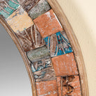 Close up image of a round mirror framed with reclaimed wood, featuring a mosaic-style border of intricately carved and coloured wooden tiles, each with unique textures and patterns, creating a rustic and artistic statement piece.
