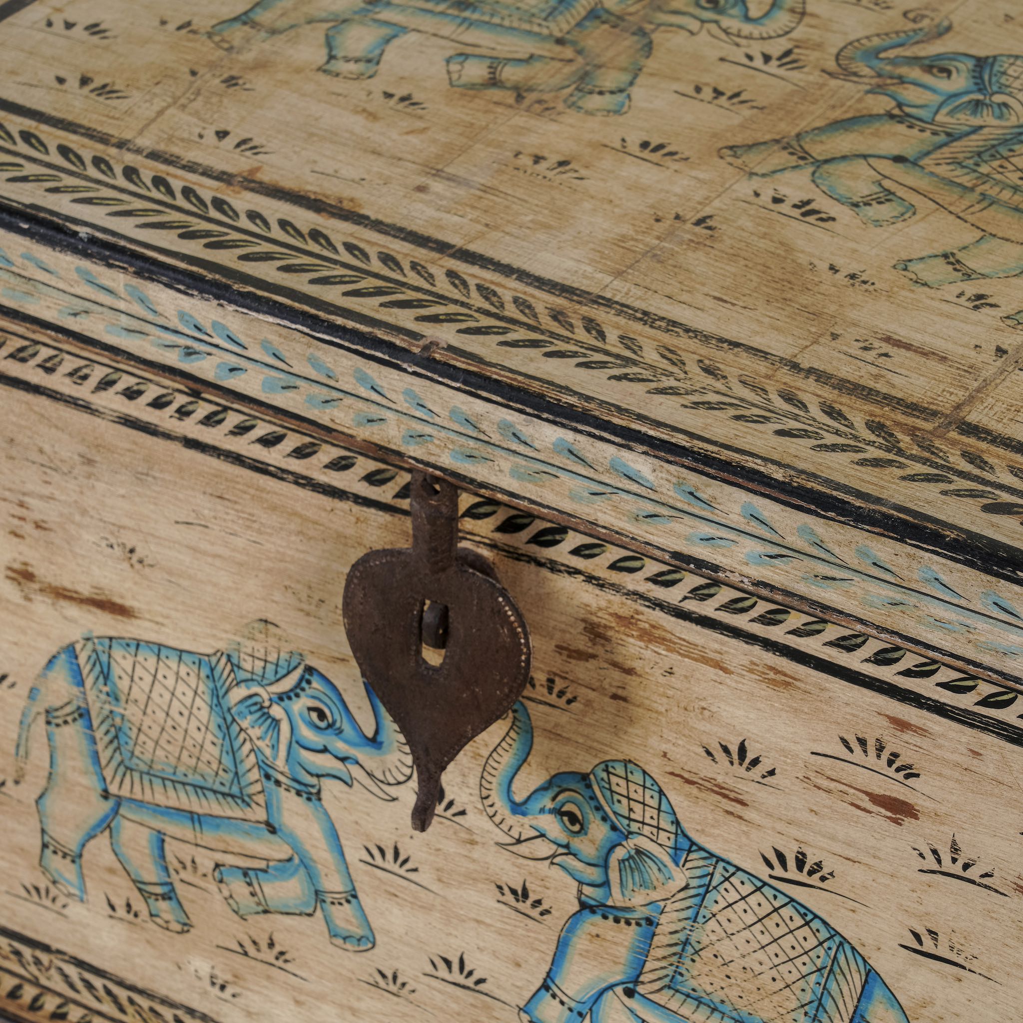 Close up image of a large hand-painted chest made from old reclaimed wood, featuring intricate blue designs of elephants and floral motifs on a distressed beige background, with a central latch and a rustic vintage finish.

